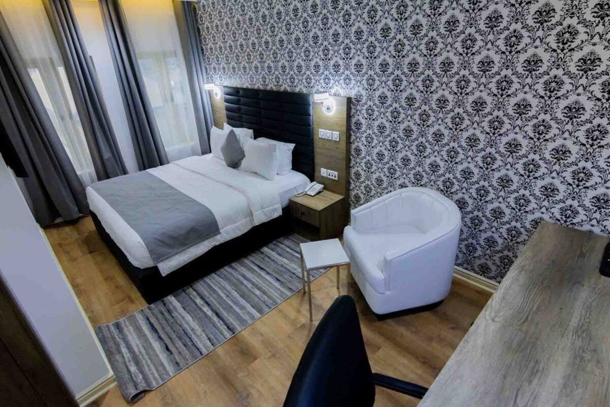 A hotel room with a large bed, a bedside table with a lamp, a chair, and a wooden desk.