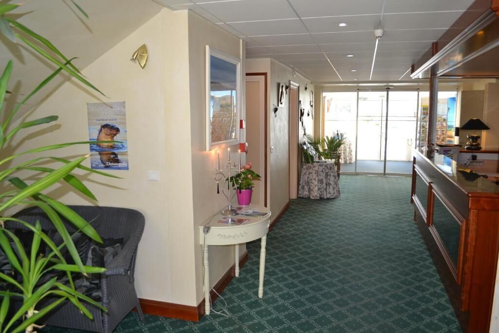 Rebuda d'hotel amb una catifa verda, una taula de recepció, zona de seients amb una cadira i una planta en test.