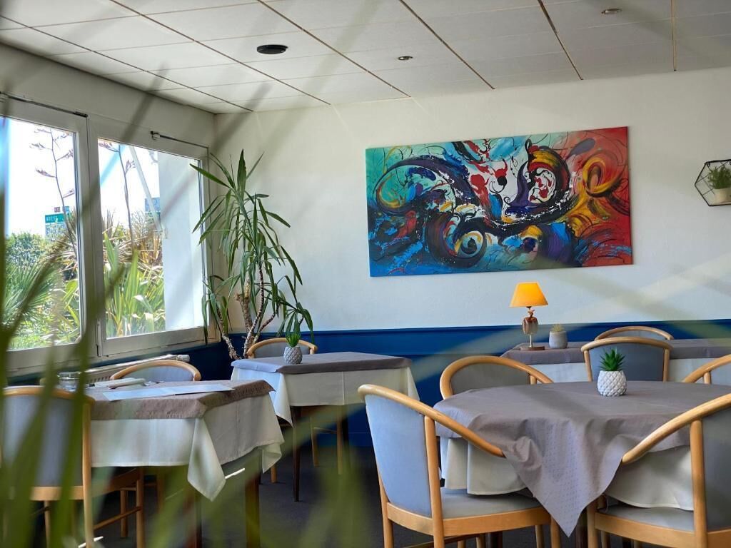 Un espace repas comprenant des tables, des chaises, une grande peinture abstraite et une plante en pot.