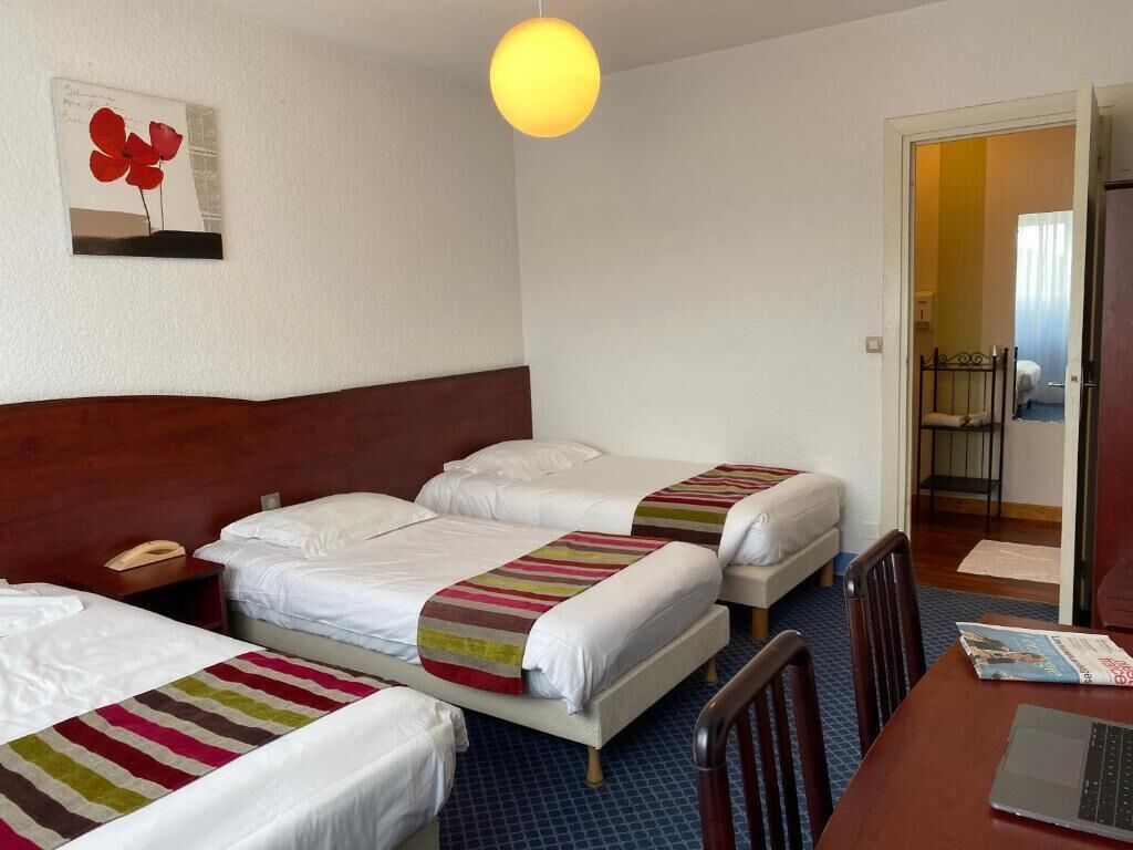 Habitación de hotel con tres camas, un escritorio, una computadora portátil, un teléfono y una obra de arte colgada en la pared.