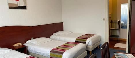 Habitación de hotel con tres camas, un escritorio, una computadora portátil, un teléfono y una obra de arte colgada en la pared.