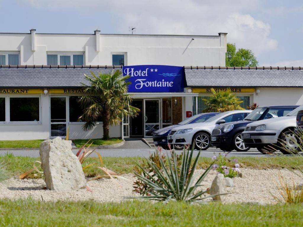 A hotel named "Hotel Fontaine" with a signboard, a parking area with cars, and a landscaped garden with rocks and plants.