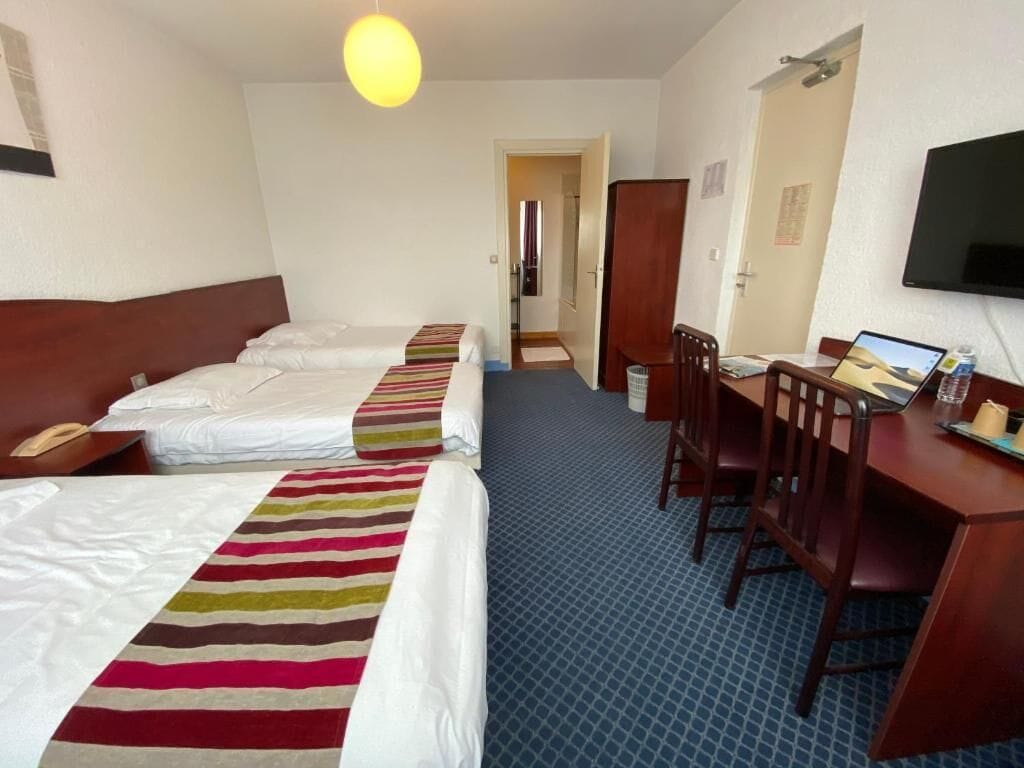 A hotel room with two beds, a desk with a chair, a television, and a bathroom visible through an open door.