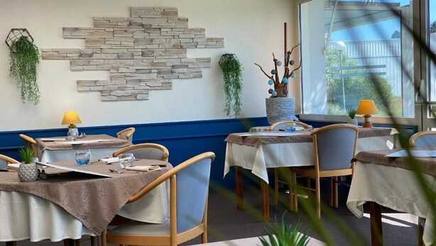 A dining area with wooden chairs and tables, a stone wall decoration, and potted plants. - Hôtel Fontaine Morlaix (Morlaix)