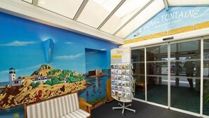 A hotel lobby with a mural of a coastal scene, a reception desk, and a seating area. - Hôtel Fontaine Morlaix (Morlaix)