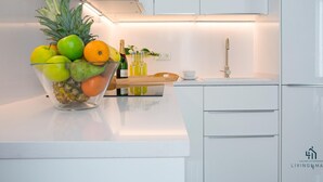 Een moderne keuken met witte kastjes, een fruitschaal op het aanrecht en een fles champagne.