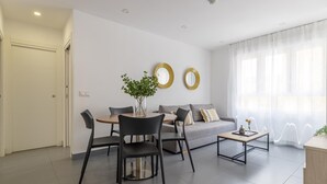 A modern living room with a sofa, two round mirrors, a coffee table, and a dining area with chairs and a table.