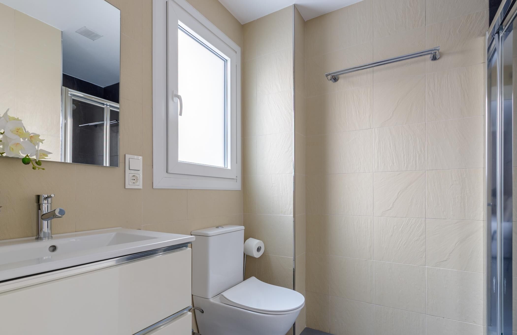 Un baño con lavamanos, espejo, inodoro y ducha.