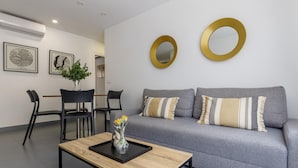 A modern living room with a grey sofa, two black chairs, a coffee table with a vase of flowers, and two gold-framed mirrors on the wall.