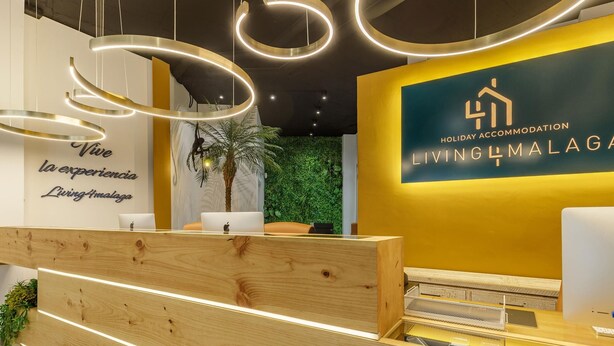 A reception desk with a wooden finish, a wall with a logo and text, and a green wall with plants.