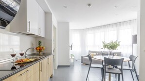 A modern kitchen with a dining area, featuring a central island, a built-in oven, and a large window providing natural light.
