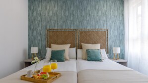 A double bed with a tray of breakfast, two bedside tables, and a window with sheer curtains.