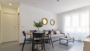 A modern living room with a sofa, two round mirrors, a coffee table, and a dining area with chairs and a table.