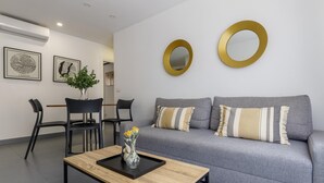 A modern living room with a grey sofa, two black chairs, a coffee table with a vase of flowers, and two gold-framed mirrors on the wall.