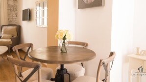 A dining area with a round table, chairs, a vase with flowers, a clock, and a stone wall.