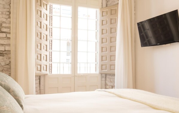 Un dormitorio con cama, televisor montado en la pared y ventana con celosía decorativa.