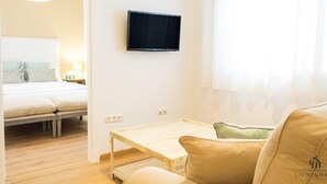 A hotel room with a bed, a TV mounted on the wall, a small table, and a window with curtains. - Mariblanca 1D Superior Living4malaga (Málaga)