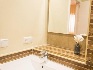 Ein Badezimmer mit einem weißen Waschbecken, einem Spiegel und einer Vase mit Blumen.