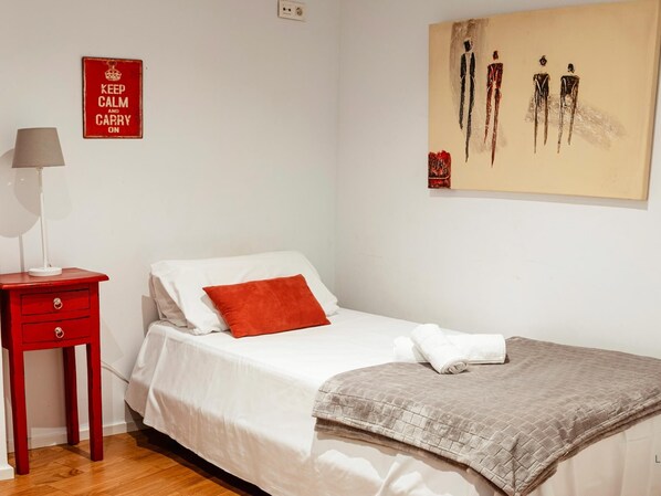A bedroom with a bed, a red nightstand, a white lamp, and a painting on the wall.