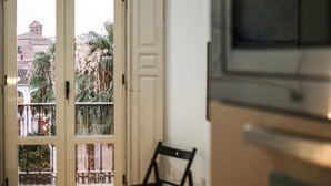 A view through a door with a balcony, a chair, and a building with a tower in the background.