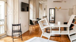 A modern living room with a dining area, wooden flooring, and a TV mounted on the wall.