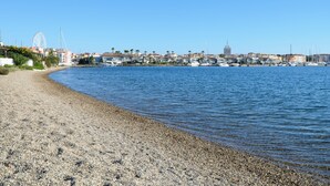 Ein Kiesstrand mit einem Yachthafen im Hintergrund, inklusive Boote und einem Riesenrad.