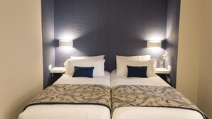 A mirrored room with two beds, each with a bedside table and lamp, and a patterned bedspread.