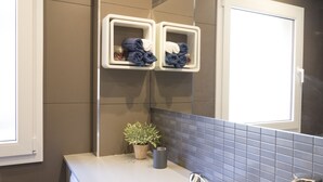A bathroom with a white countertop, a sink with a modern faucet, a potted plant, and two towel racks with folded towels.