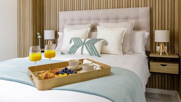 Un lit bien fait, avec des oreillers, une table de chevet avec une lampe et un plateau contenant des éléments pour le petit-déjeuner.