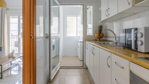 Une cuisine moderne avec des meubles blancs, un plan de travail en bois, un four à micro-ondes et un panier de fruits.