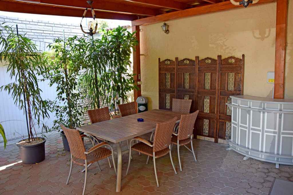 An outdoor patio with a table and chairs, surrounded by potted plants and a decorative wooden screen.