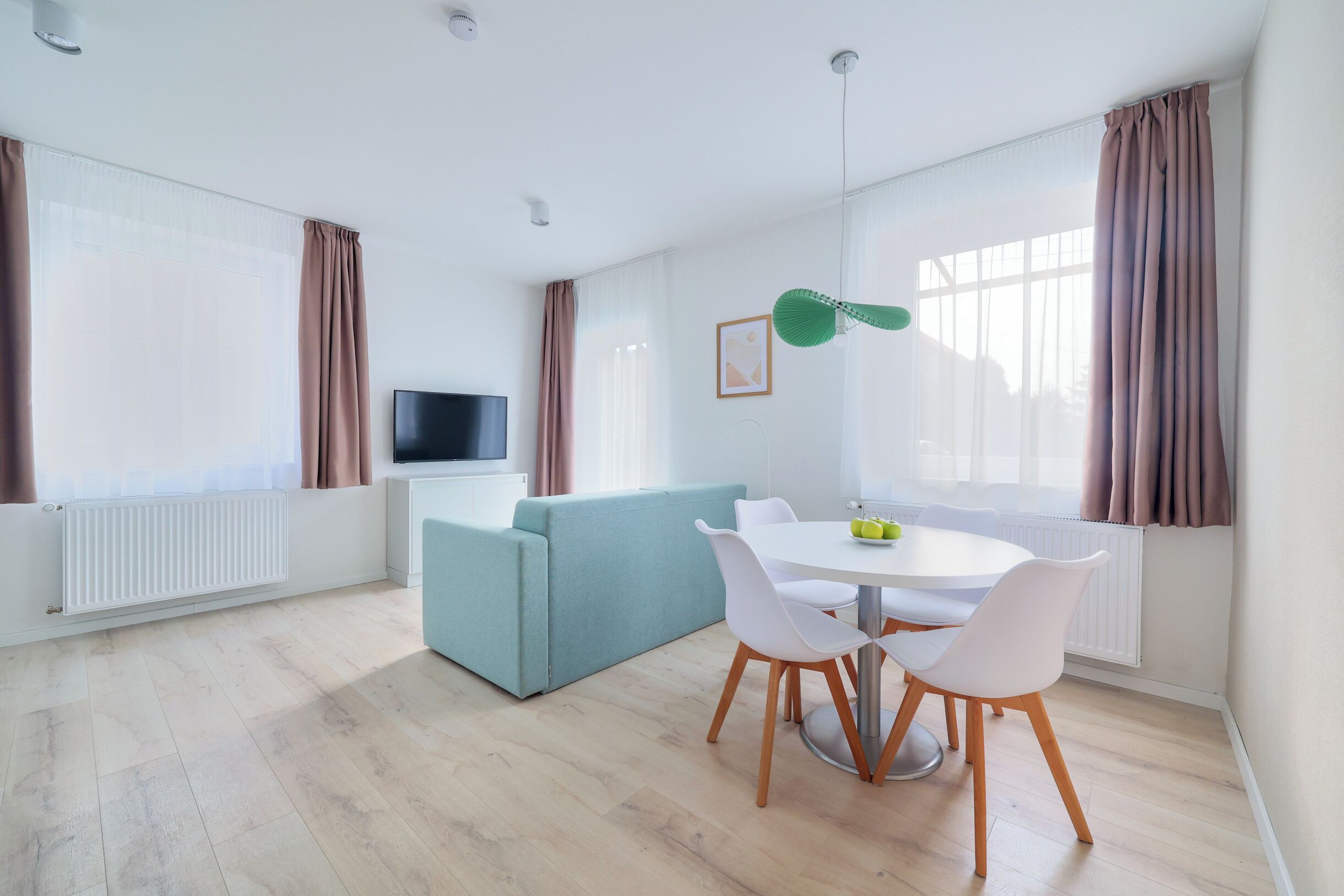 A modern living room with a sofa, a dining table with chairs, a flat-screen TV, and a window with curtains.