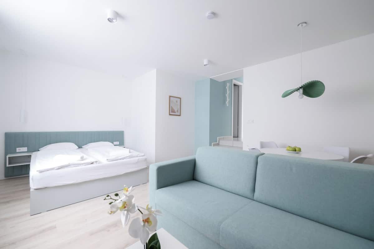 A modern bedroom with a bed, a light blue sofa, a small table, and a mirror.