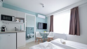 Una habitación de hotel moderna con cama, escritorio, microondas, televisor y una pequeña mesa con sillas.