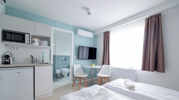 Una habitación de hotel moderna con cama, escritorio, microondas, televisor y una pequeña mesa con sillas.