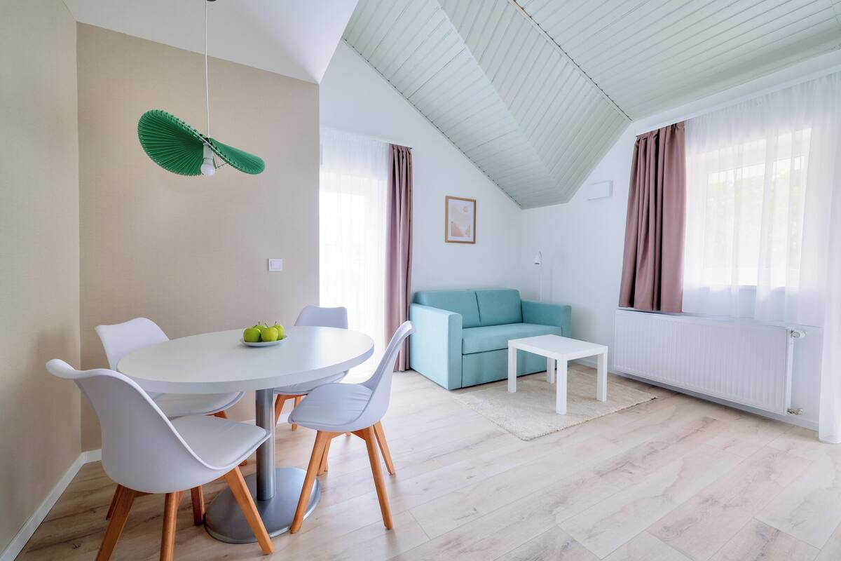 A modern living room with a light blue sofa, a white dining table with chairs, and a hanging green light fixture.