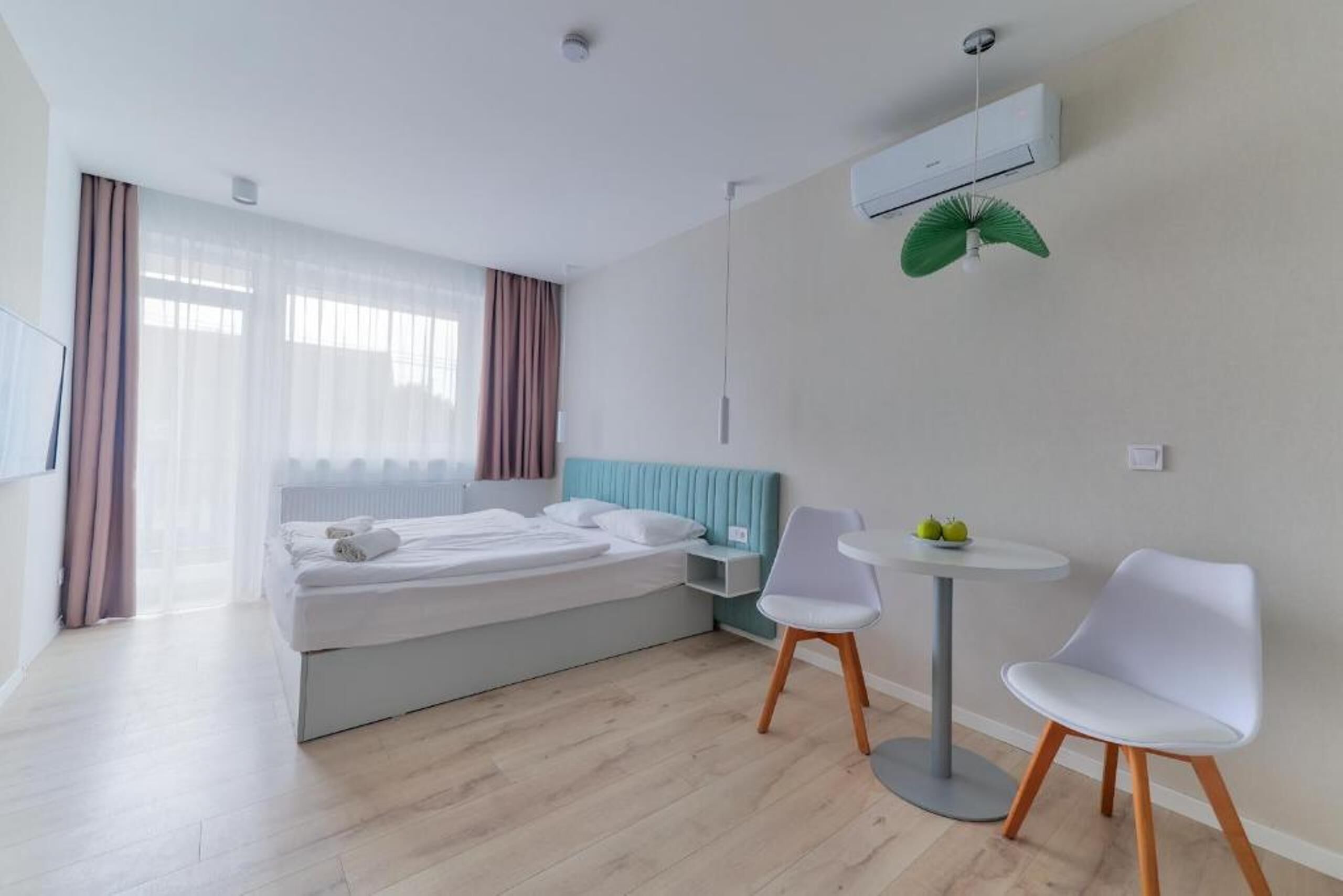 Una habitación de hotel moderna con cama, una pequeña mesa con sillas, televisor y aire acondicionado.
