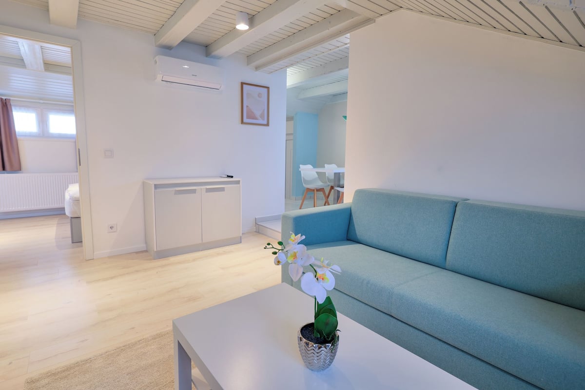 A modern living room with a sofa, a coffee table with a potted orchid, and a dining area with chairs and a table.