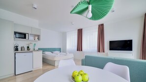 Habitación de hotel moderna con kitchenette, una cama, un televisor y un comedor con un plato de manzanas.