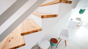 Un interior moderno con una escalera, paredes blancas y un área de comedor con sillas y una mesa.