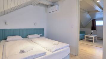 Ein Schlafzimmer mit zwei Betten, einem blauen Kopfteil, einem kleinen Tisch mit Pflanze und einem Fenster mit Vorhängen.