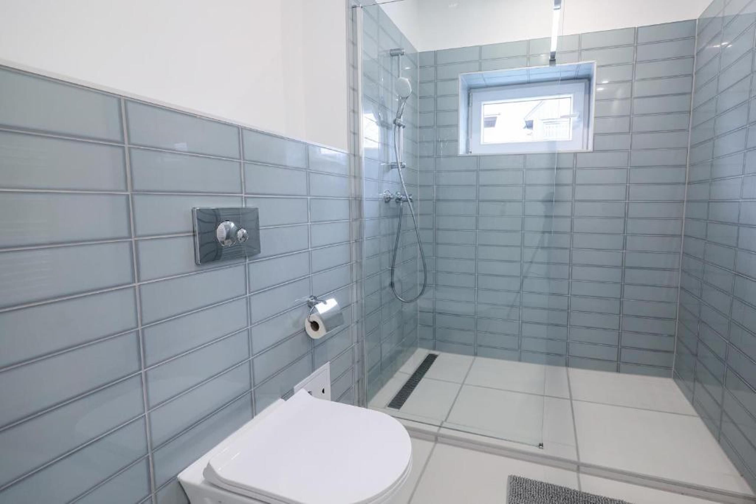 A bathroom with a glass shower enclosure, a toilet, and a small window.