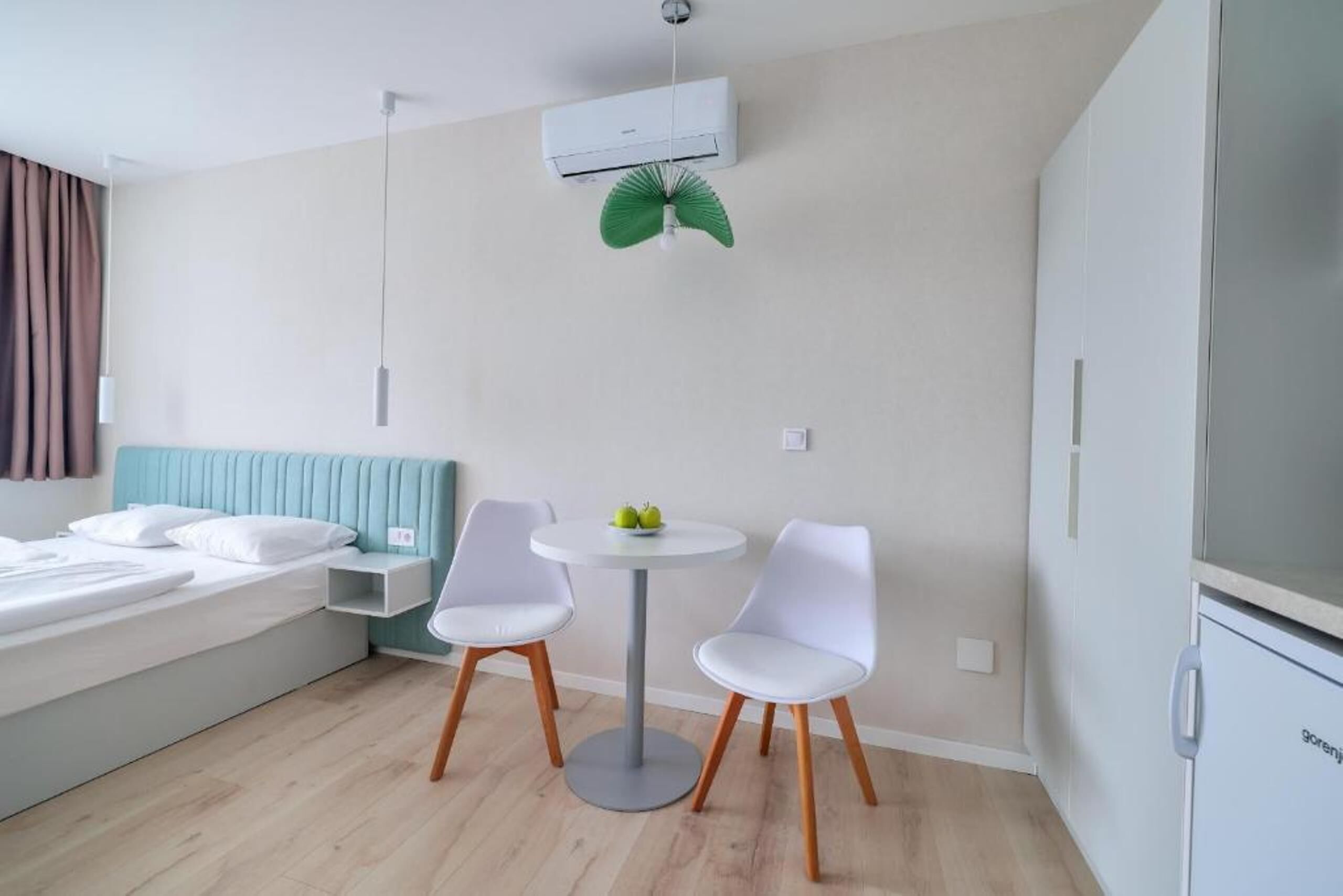 A modern bedroom with a bed, a bedside table, a small round table with two chairs, and an air conditioning unit.