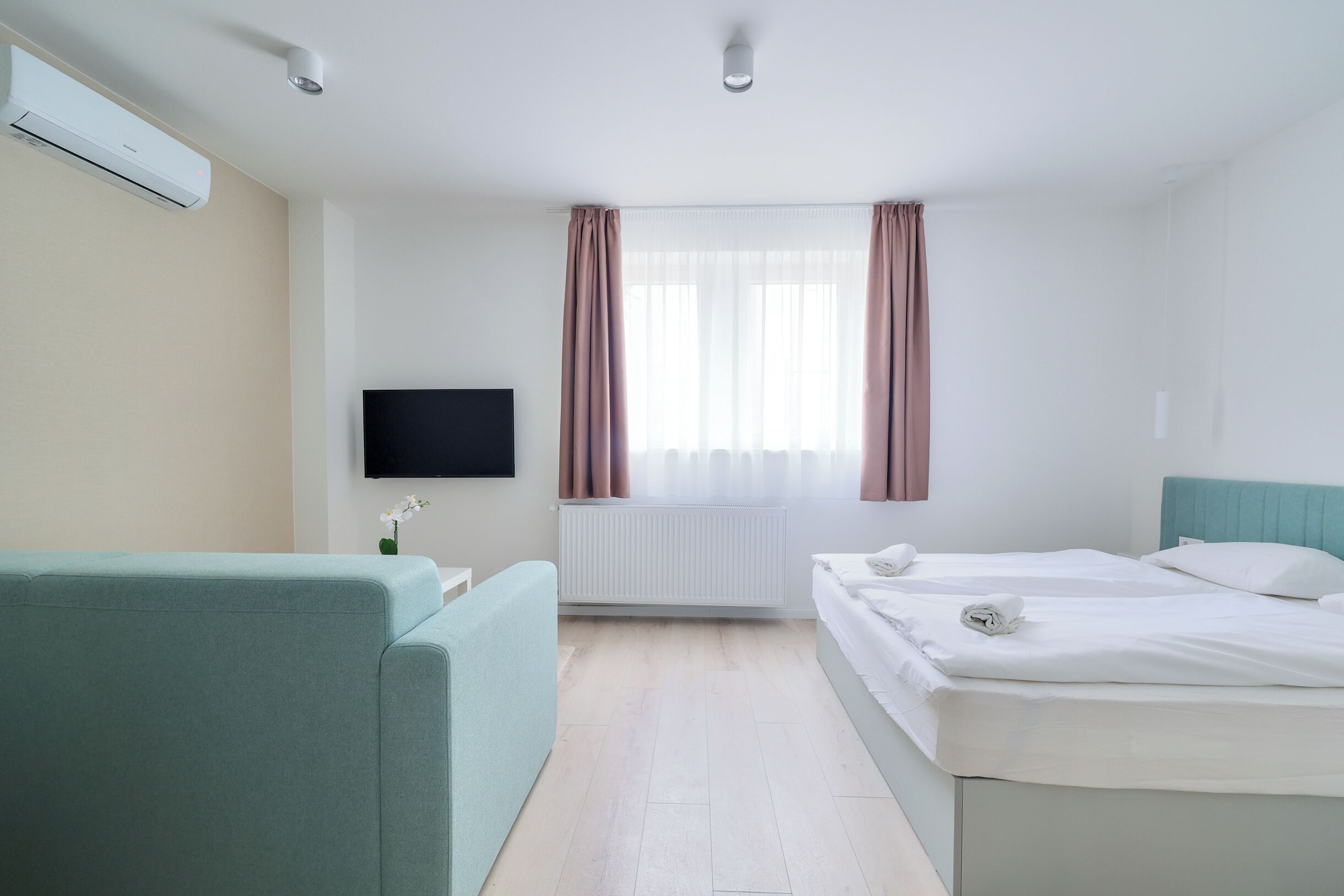 Una habitación de hotel con una cama, un sofá, un televisor y una ventana con cortinas.