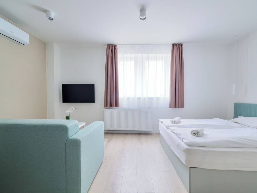 Una habitación de hotel con una cama, un sofá, un televisor y una ventana con cortinas.