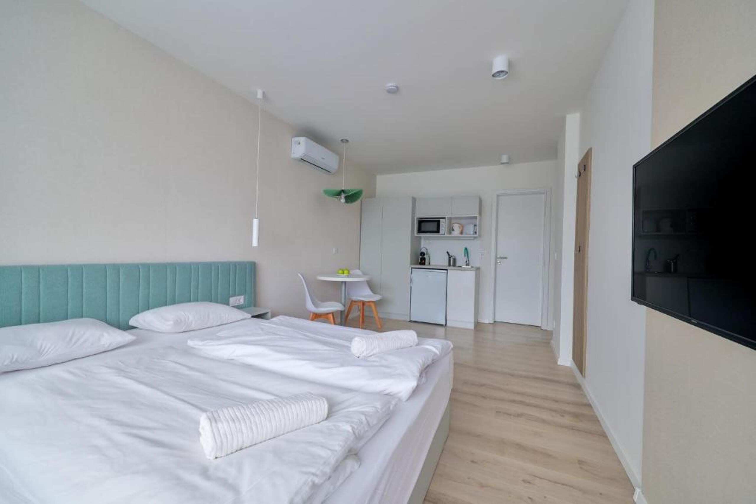 A modern hotel room with a large bed, a small kitchenette, and a TV mounted on the wall.