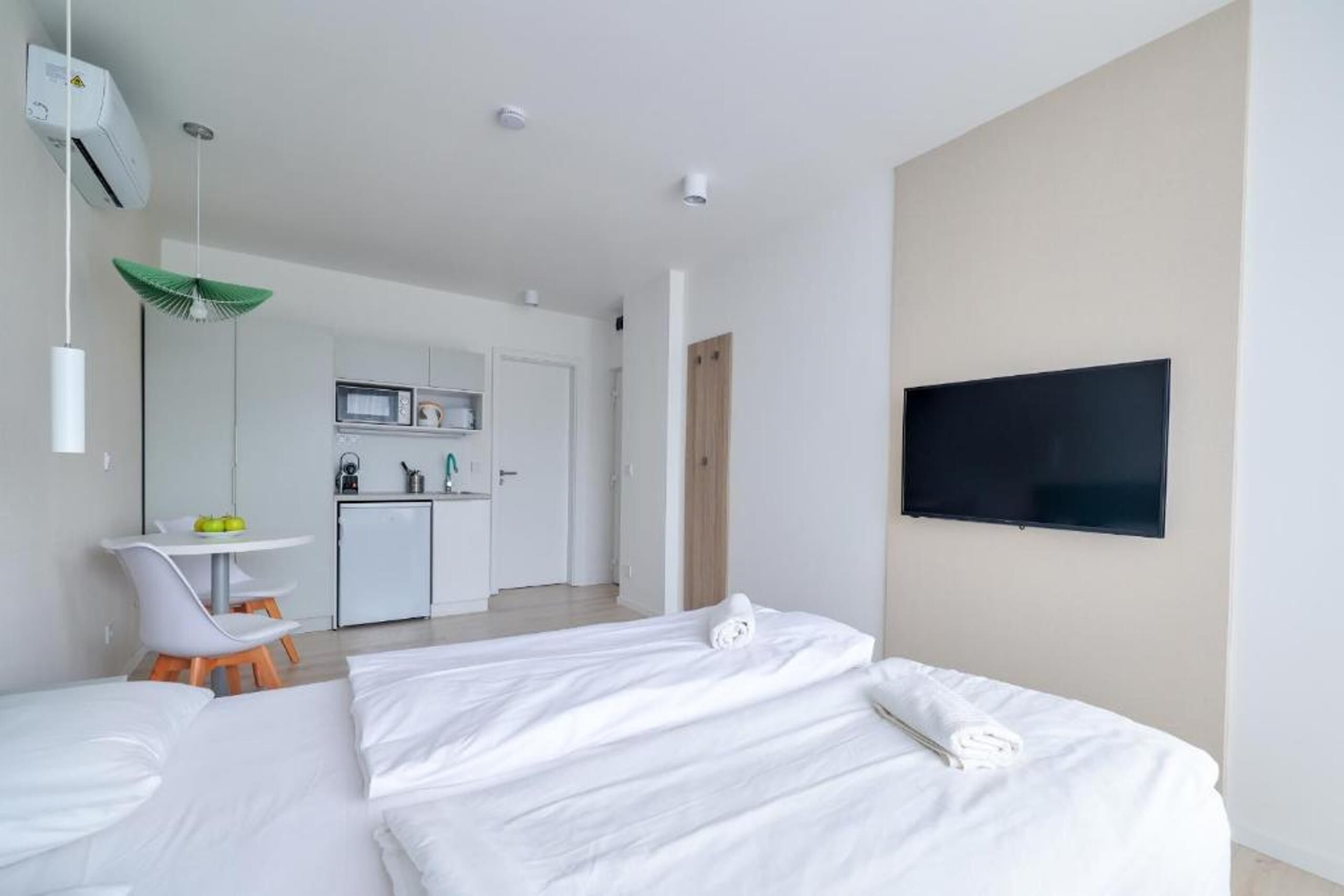 Una habitación de hotel moderna con dos camas, televisión, kitchenette y zona de comedor.
