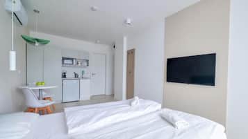 Una habitación de hotel moderna con dos camas, televisión, kitchenette y zona de comedor.
