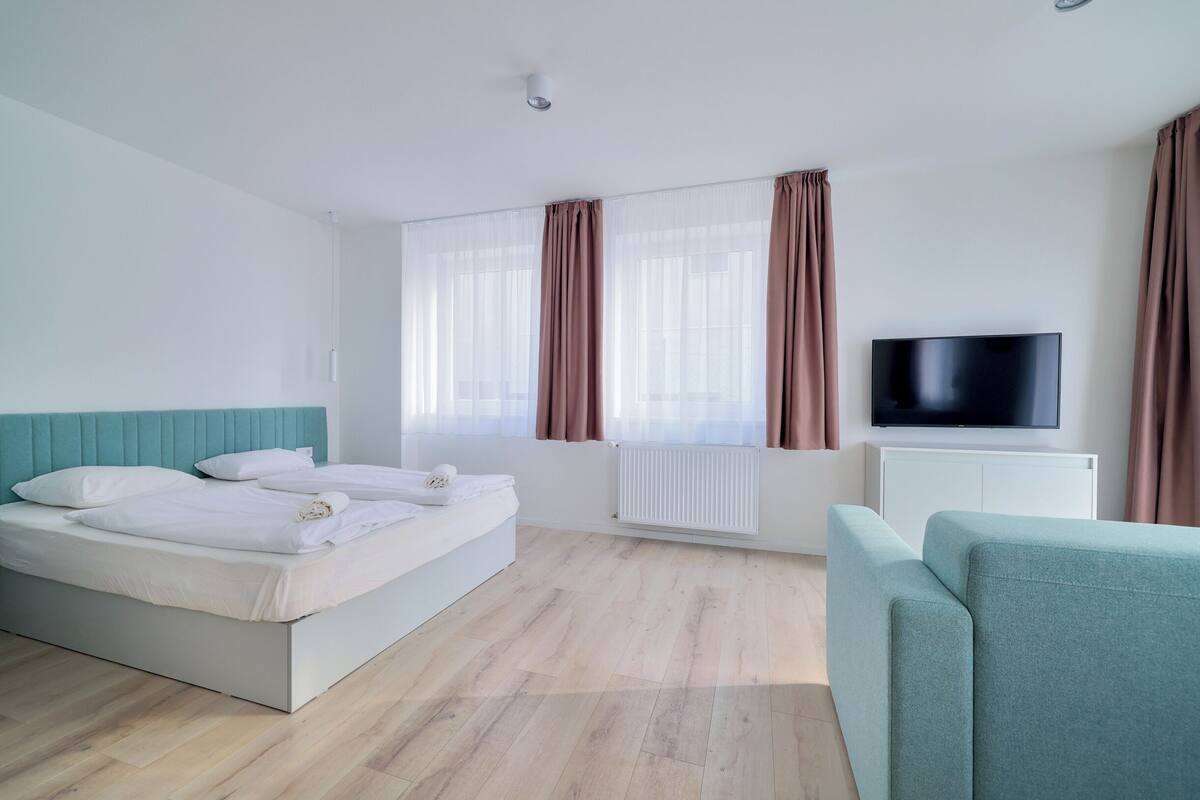 A modern hotel room with a large bed, a TV, and a sofa.