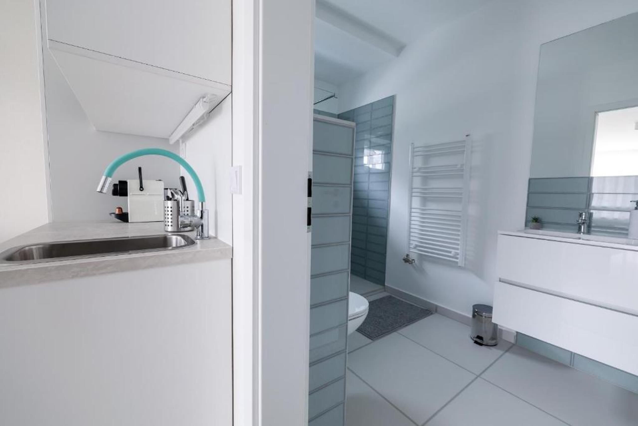 Un baño moderno con cabina de ducha de vidrio, un lavabo blanco con espejo curvo y un mueble de tocador blanco con un espejo grande.